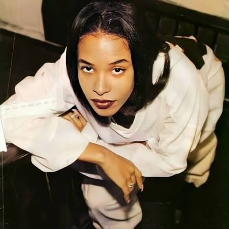 A young Aaliyah photographed from above in an oversized cream hooded sweatshirt, looking up into the camera.
