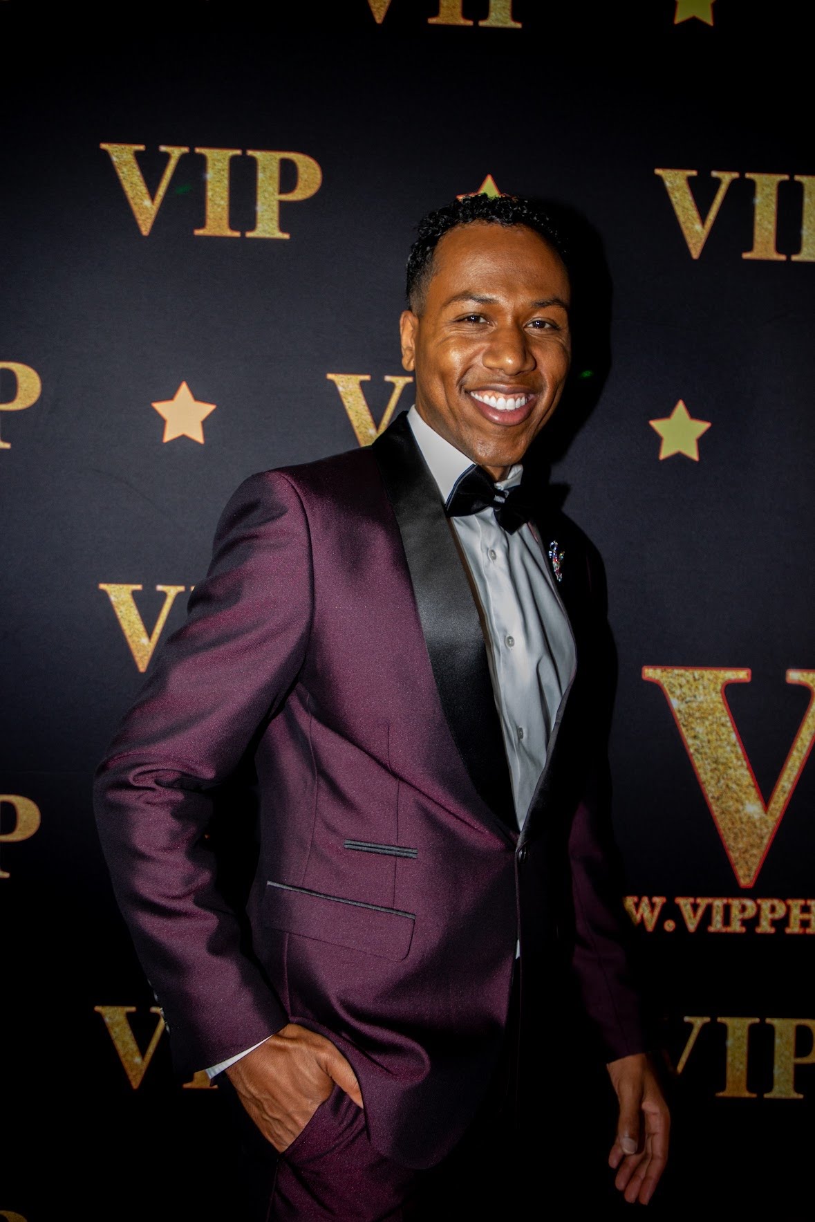 Aaron The Uplifter on the step-and-repeat in a burgundy tuxedo at the Black Beat Magazine relaunch event.