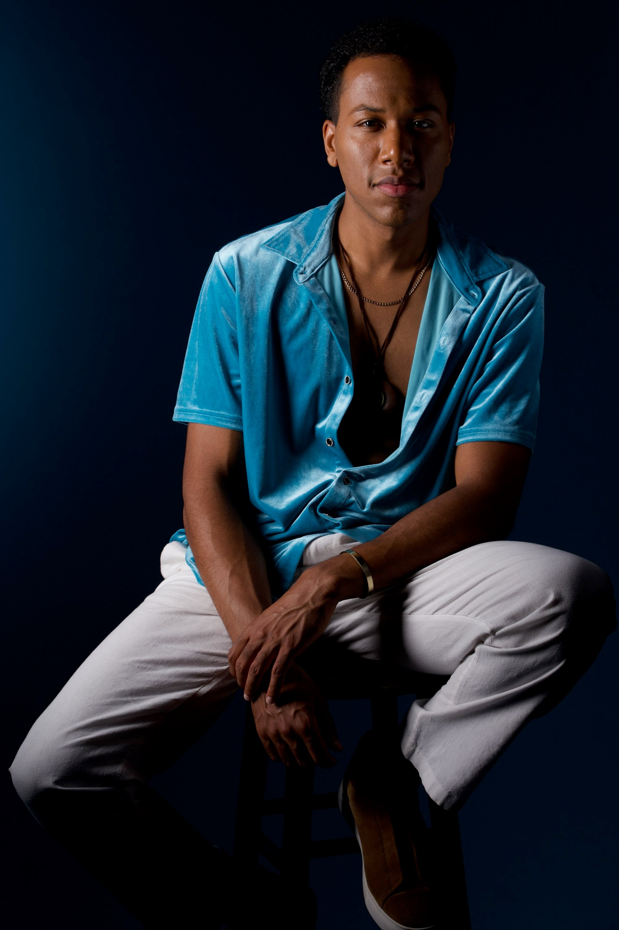 Aaron The Uplifter seated in a teal velvet shirt against a deep blue backdrop.