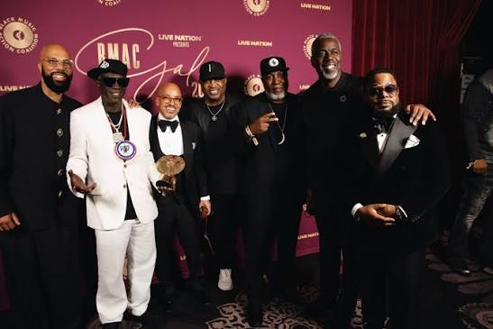 Members of Public Enemy, including Flavor Flav in a white suit, posing with Common and guests at the BMAC Gala 2026