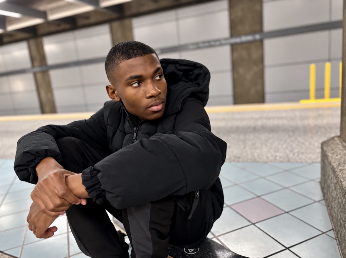 Christopher Bates in a black puffer jacket crouched on a subway platform.