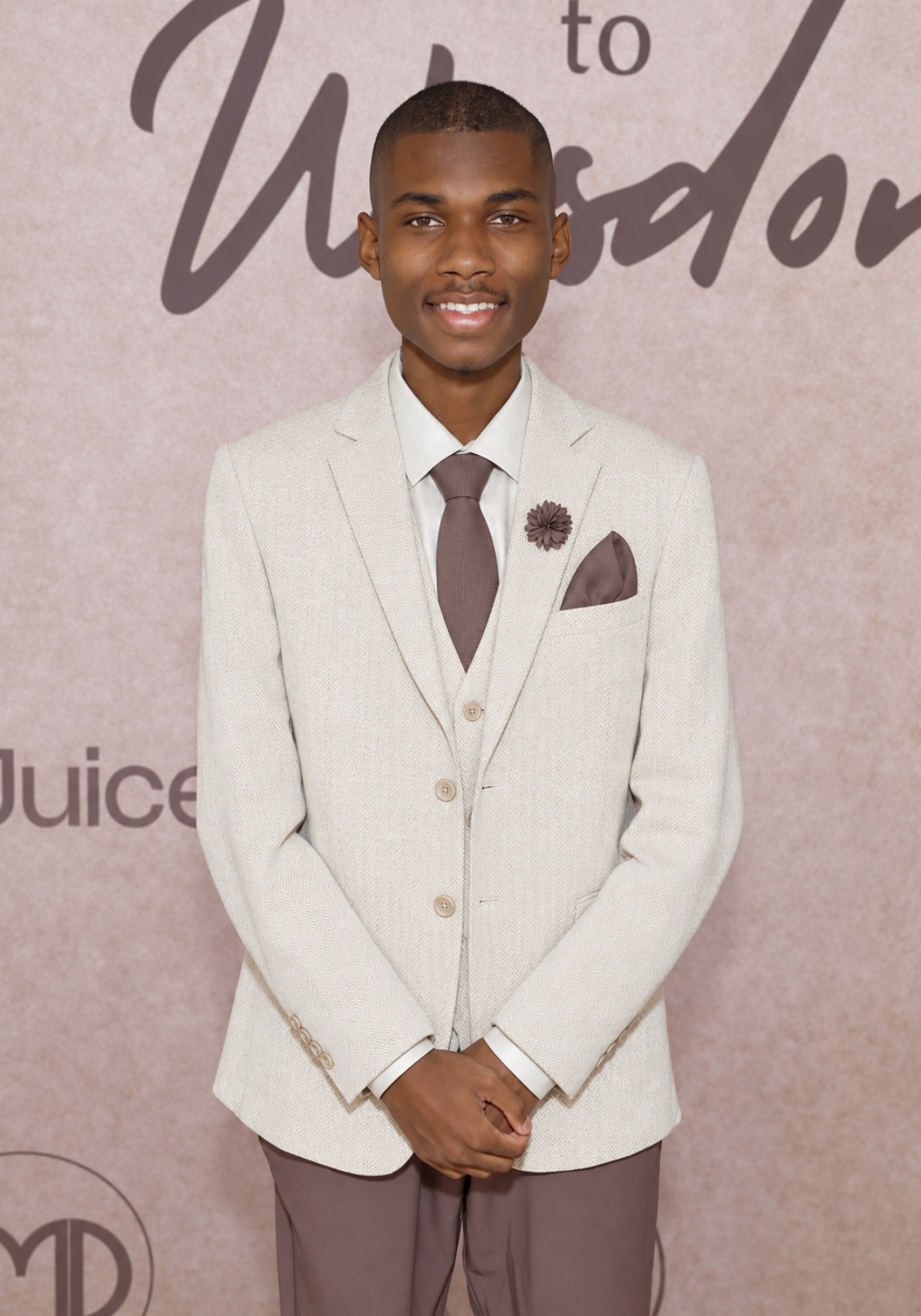Christopher Bates on a red carpet in a cream herringbone three-piece suit with a mauve tie and pocket square.