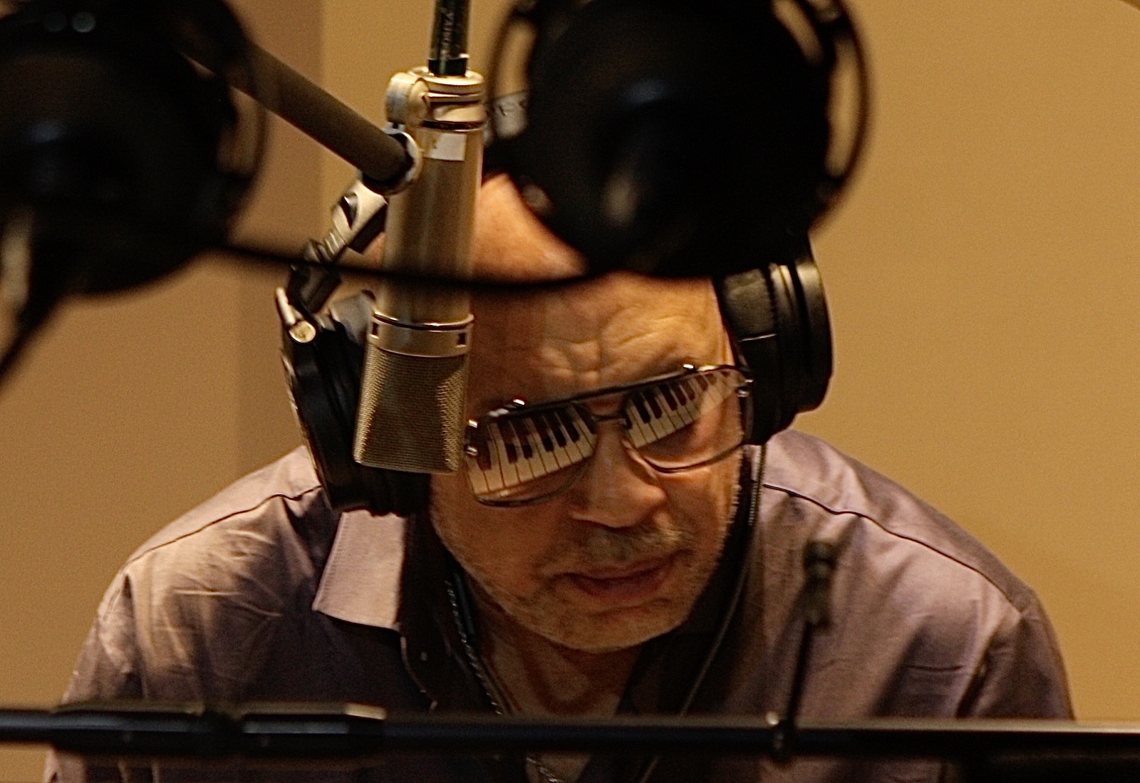 Frank McComb in the studio, wearing headphones and sunglasses that reflect a set of piano keys.