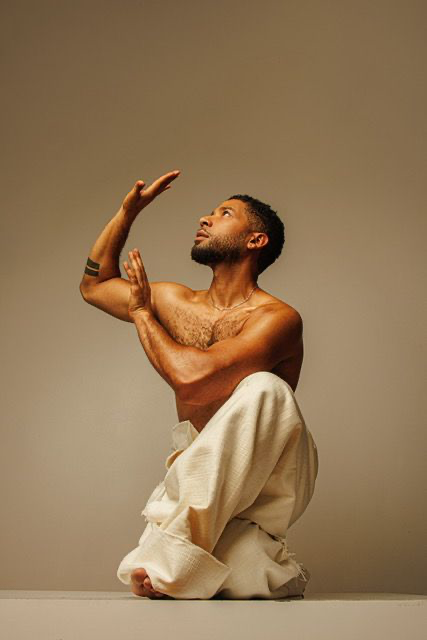 Jussie Smollett in an expressive movement pose, arm raised, photographed in a warm-toned studio.