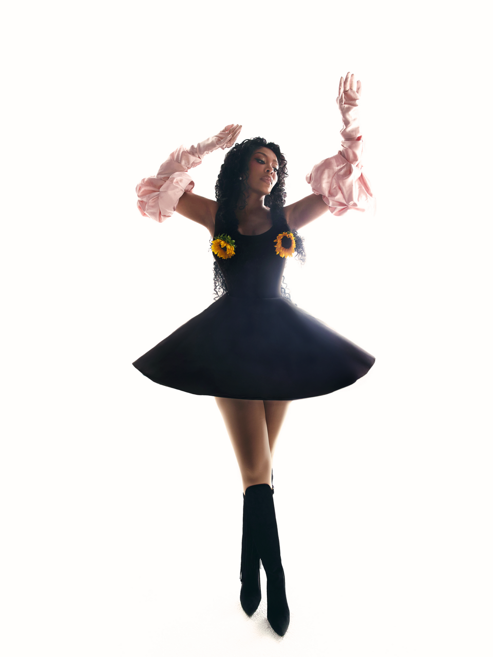 Full-length editorial portrait of K. Michelle in a black dress with sunflowers and pink gloves.