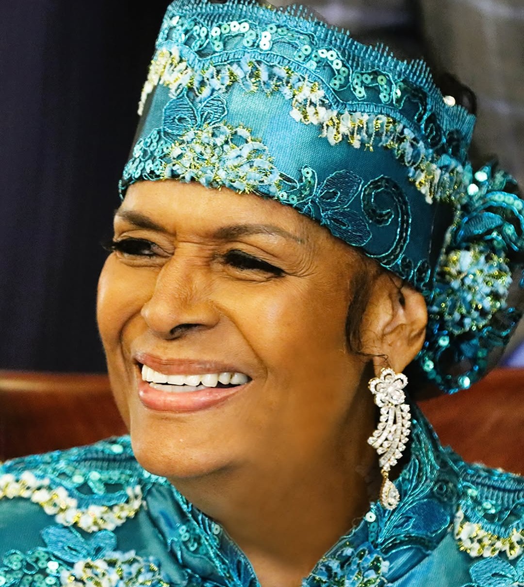 A radiant portrait of Mother Khadijah Farrakhan smiling, wearing an ornate teal headpiece.