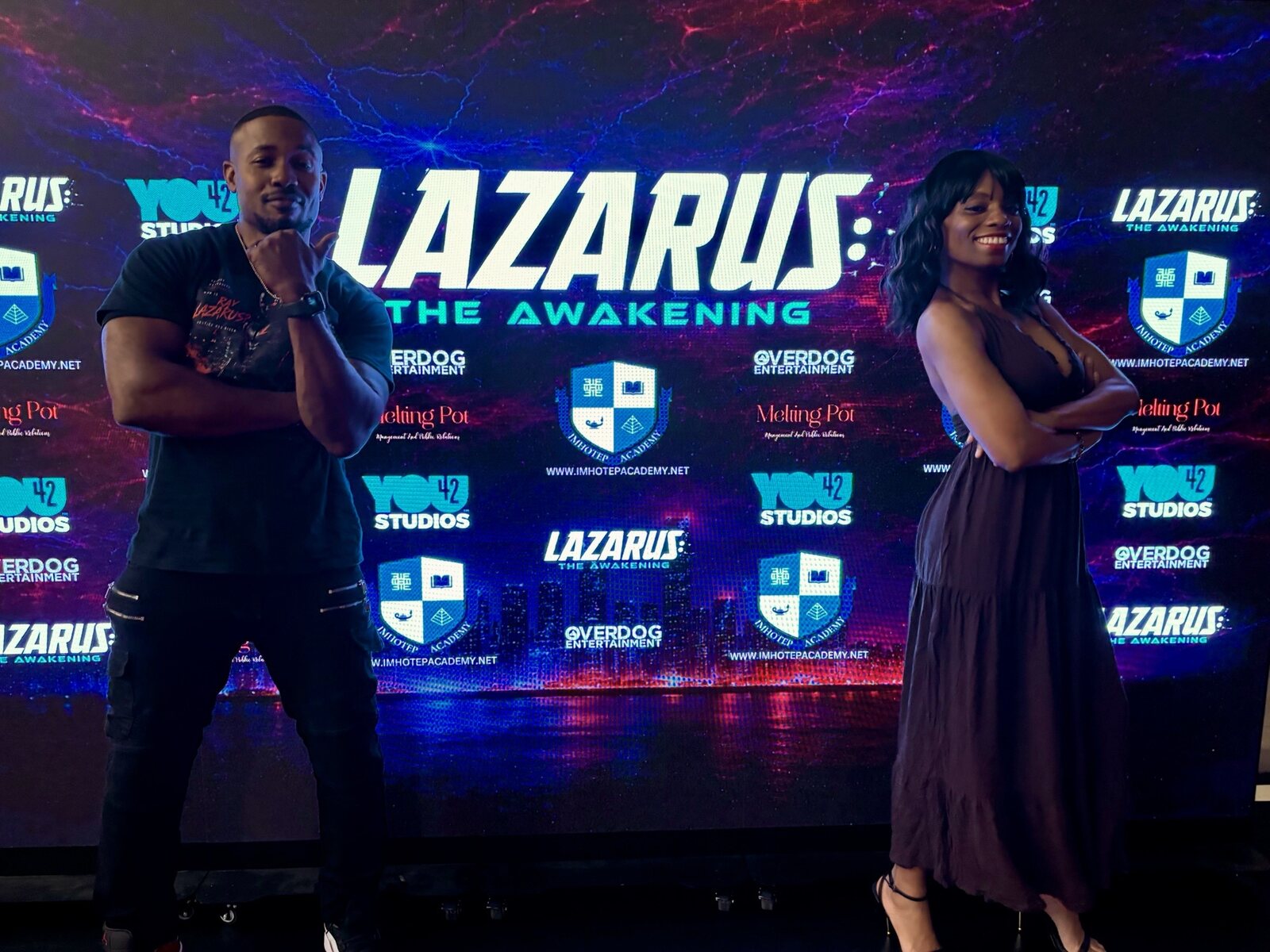 Two guests posing in front of the Lazarus: The Awakening step-and-repeat backdrop at You42 Studios.