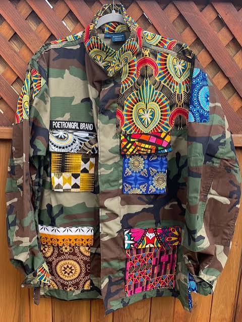 A PoetRoniGirl Army Couture jacket: a woodland camouflage field jacket layered with African wax-print fabrics, kente panels and hand-placed patches in red, gold, blue and pink.