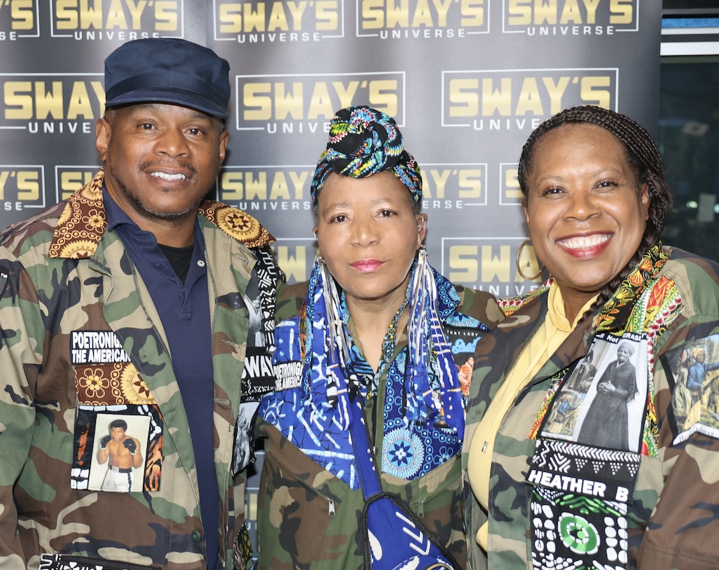 PoetRoniGirl, center, in a head wrap and blue African-print jacket, flanked by two people wearing her camouflage jackets&mdash;one bearing a Muhammad Ali portrait, the other a Harriet Tubman panel reading &lsquo;We Will Not Be Erased.&rsquo;