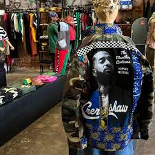 A PoetRoniGirl Army Couture jacket displayed on a mannequin, featuring a large Nipsey Hussle portrait and a &lsquo;Crenshaw&rsquo; panel set against African-print fabric.