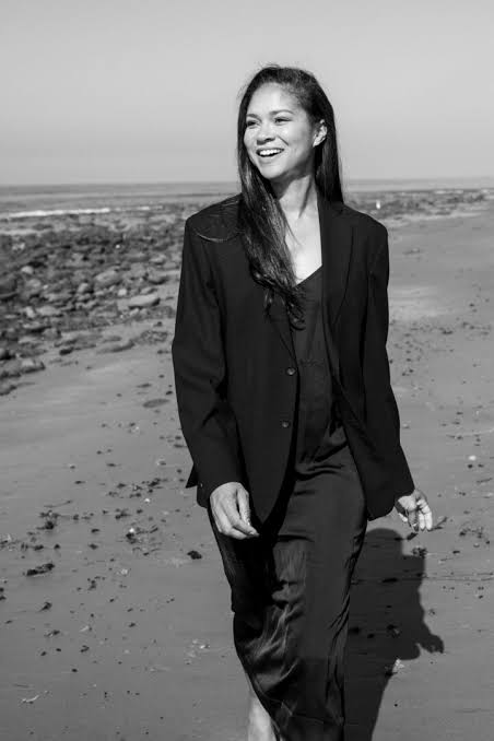 Shireen Crutchfield walking along a beach, smiling, in a black blazer and slip dress.
