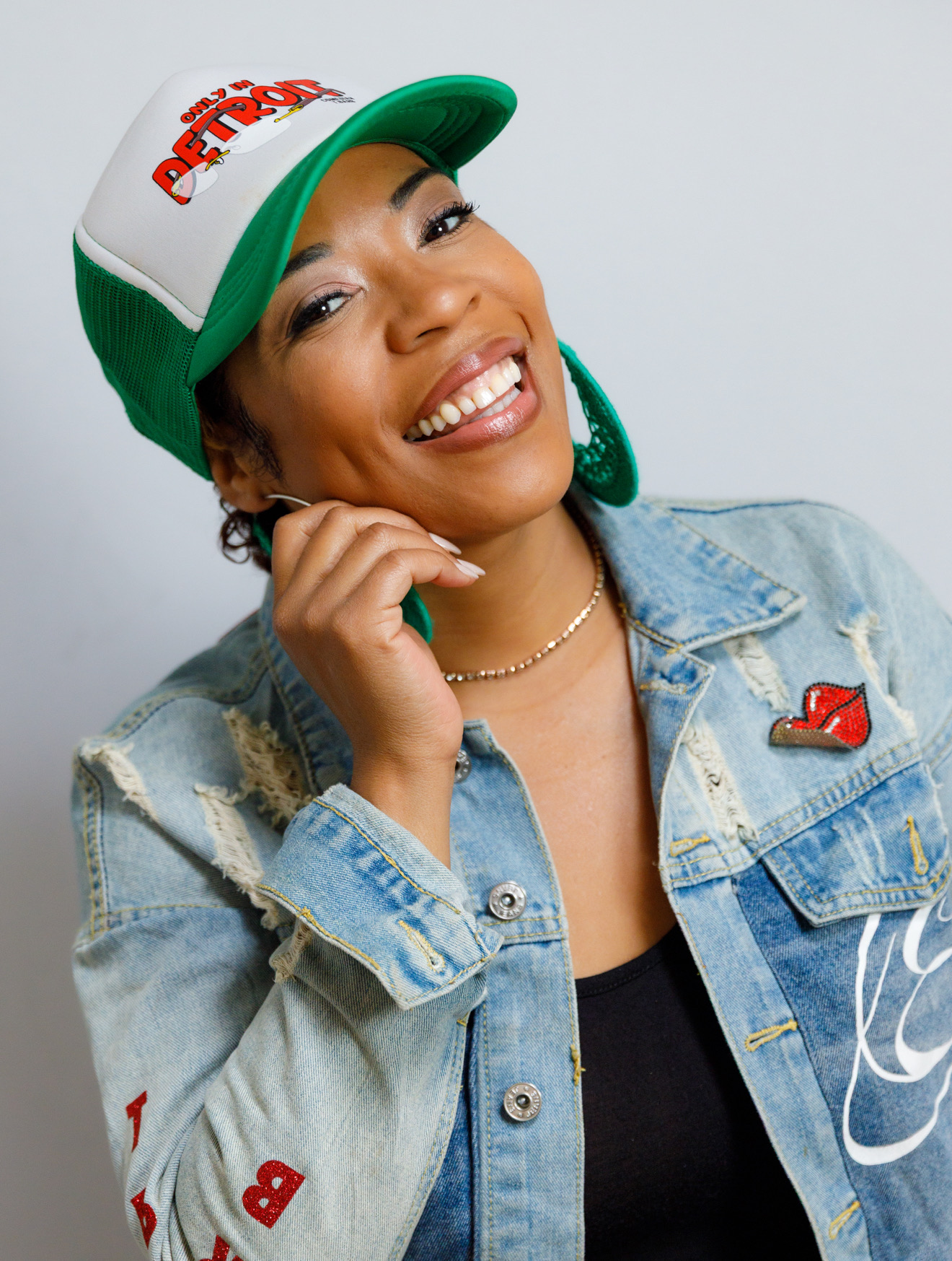 Comedian Tiffany &ldquo;T.Barb&rdquo; Barber smiling in an &ldquo;Only In Detroit&rdquo; trucker cap and a customized denim jacket.