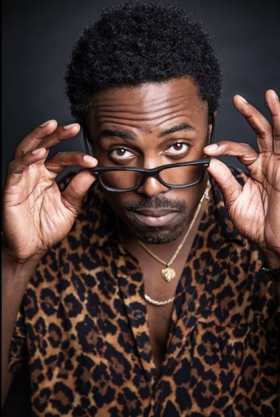 Willie Macc adjusting his glasses in a studio portrait.